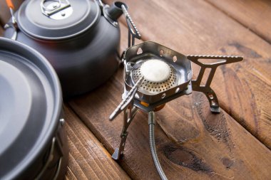 Masanın üzerinde duran turist gazı ocağı ve çatal bıçak.