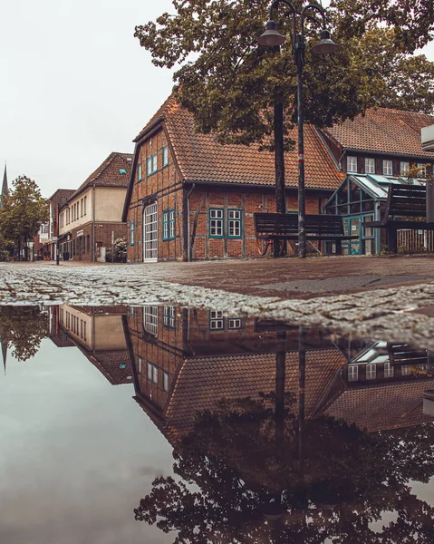 Büyük bir su birikintisi yansıması ile bir kasaba sokakta yarı ahşap ev