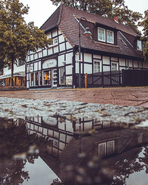 Büyük bir su birikintisi yansıması ile bir kasaba sokakta yarı ahşap ev