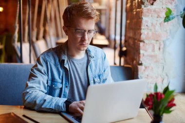 Genç adam kafede dizüstü bilgisayarüzerinde çalışıyor.