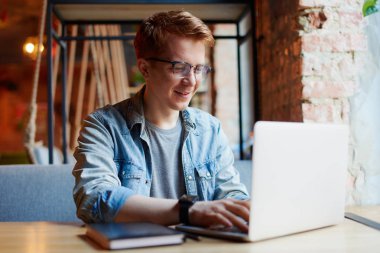 Genç adam kafede dizüstü bilgisayarüzerinde çalışıyor.