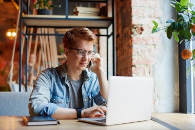 Genç adam kafede dizüstü bilgisayarüzerinde çalışıyor.