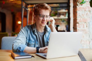 Genç adam kafede dizüstü bilgisayarüzerinde çalışıyor.