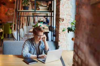 Genç adam kafede dizüstü bilgisayarüzerinde çalışıyor.