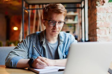 Genç adam kafede dizüstü bilgisayarüzerinde çalışıyor.