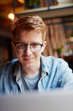 Genç adam kafede dizüstü bilgisayarüzerinde çalışıyor.