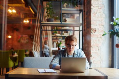 Genç adam kafede dizüstü bilgisayarüzerinde çalışıyor.