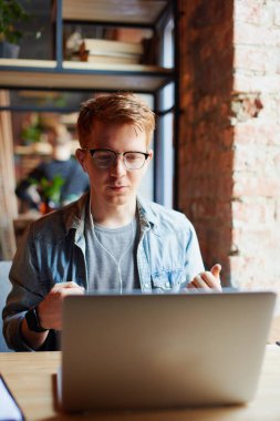 Genç adam kafede dizüstü bilgisayarüzerinde çalışıyor.