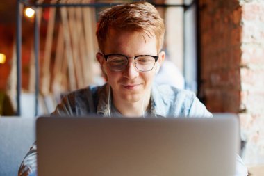 Genç adam kafede dizüstü bilgisayarüzerinde çalışıyor.