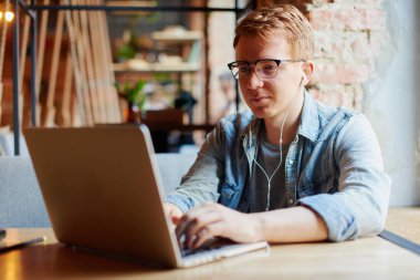 Genç adam kafede dizüstü bilgisayarüzerinde çalışıyor.