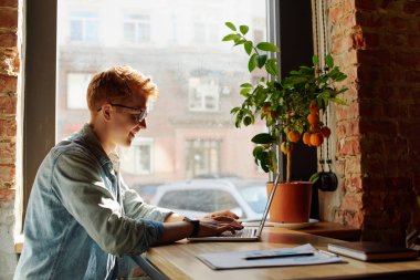 Genç adam kafede dizüstü bilgisayarüzerinde çalışıyor.