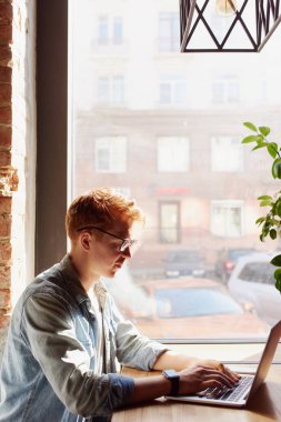 Genç adam kafede dizüstü bilgisayarüzerinde çalışıyor.