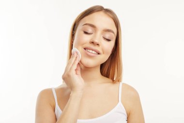 Gülümseyen kız beyaz bir arka plan üzerinde pamuklu bir bez ile yüzünü siler