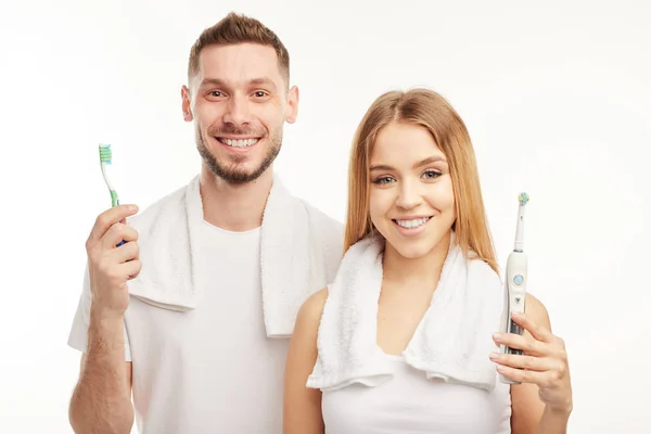 Hombre y mujer sonrientes sosteniendo cepillos de dientes sobre un fondo blanco — Foto de Stock