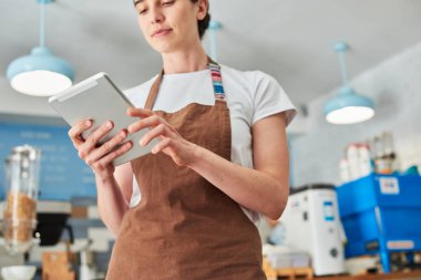 Tablet ile çalışan kahverengi önlük Barista.