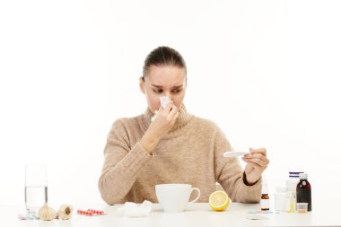 Hasta kadın tıbbi temin ile çevrili masada oturur ve termometre bakar.