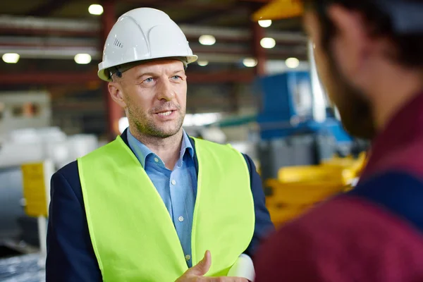 Inżynierowie w twardych kapeluszach rozmawiają ze sobą w zakładzie przemysłowym. — Zdjęcie stockowe