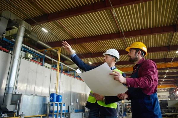 Ingenieros con sombreros duros sostienen el plano mientras discuten la situación en la planta . — Foto de Stock