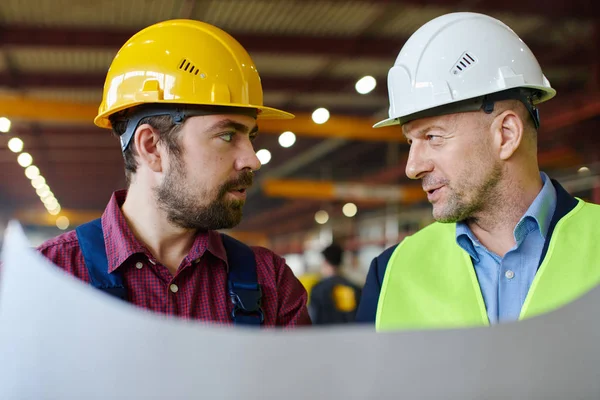 Ingenieure mit harten Hüten schauen einander an, während sie einen Bauplan in der Hand halten. — Stockfoto