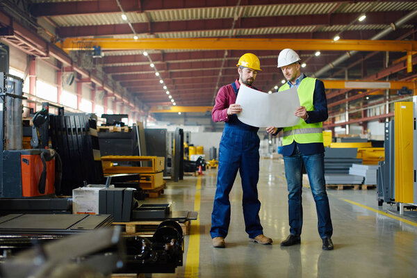 Engineers in hard hats working on a blueprint at the industrial plant.