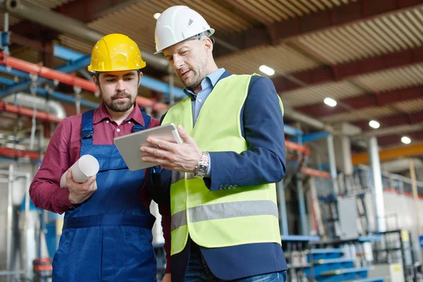 Engenheiros em chapéus duros olhando para a tela de um tablet . — Fotografia de Stock