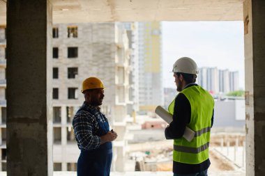 İki mühendis, katlanmış planı tutan birlikte iş ilgili soruları tartışmak.