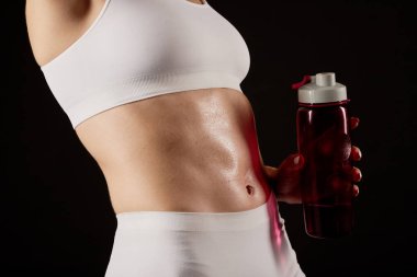 Kamerada altı paketi gösteren ve bir su şişesi tutan spor kıyafetinde bir kadının yakın.