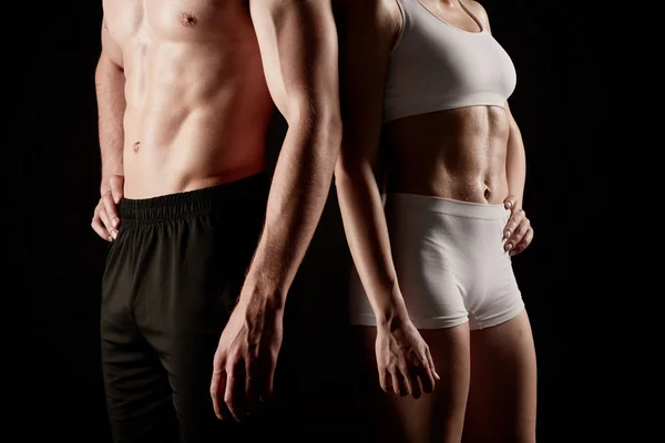 Fit couple in sportswear poses at the camera standing close together in a close-up.