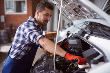 Adam kırık bir araba motoru fiksasyon altında araba servisinde çalışıyor.