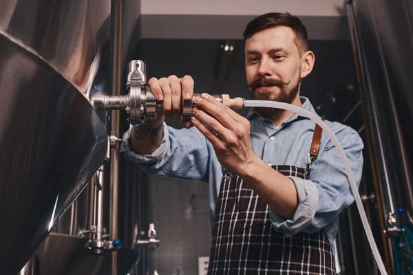 Trabalhador da cervejaria adiciona mais cerveja para o barril maior de um menor . — Fotografia de Stock