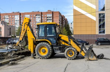 Sarı traktör iş başında, borular için çukur kazıyor.
