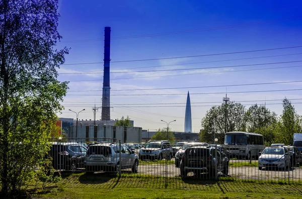フェンスの後ろの駐車場の背景に都市 大きなパイプと大きな超高層ビルの眺め — ストック写真