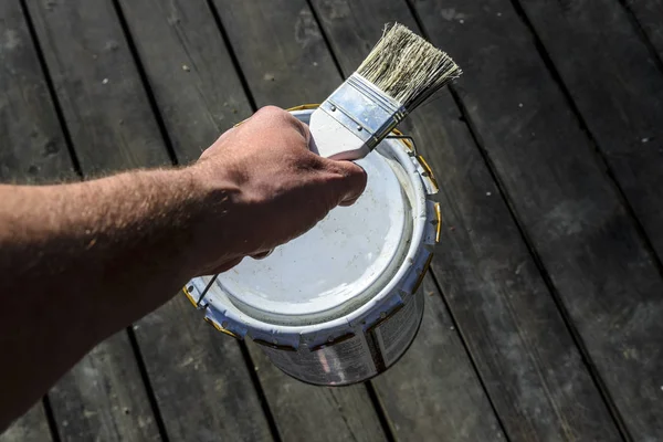 a man with a strong hand carries a can of paint over the terrace and holds a brush, repair in a private house, a working painter plasterer