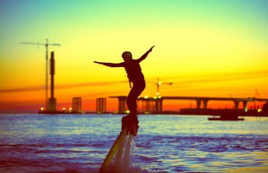 flyboard in the night sky of St. Petersburg. flying and flitting over the water people, on the background of a beautiful sunset, the outgoing sun and the background of the city. clipart