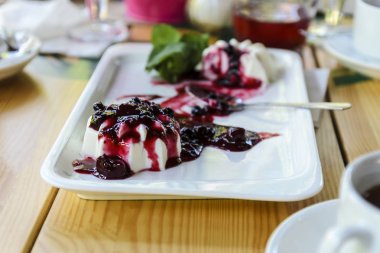 beyaz dikdörtgen plaka üzerinde panacota, krem ve reçel tatlı ahşap bir masa üzerinde duran, yemeklerin arka planda.