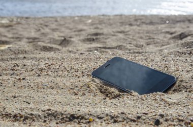 kumda sahilde yatan cep telefonu. hava koşullarına dayanıklı telefonlar, kayıp telefon konsepti, veri kaybı.