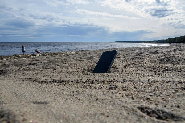 kumda sahilde yatan cep telefonu. hava koşullarına dayanıklı telefonlar, kayıp telefon konsepti, veri kaybı.