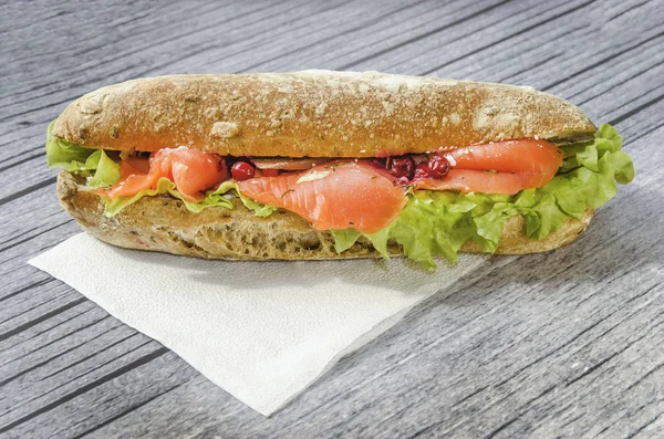 big and hearty sandwich with red fish, salmon fillet, salad, cranberry and fresh bun. the concept of lunch. on a wooden gray background. wood texture