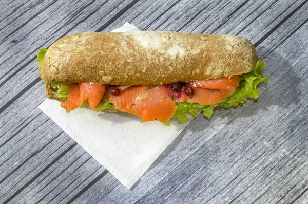 big and hearty sandwich with red fish, salmon fillet, salad, cranberry and fresh bun. the concept of lunch. on a wooden gray background. wood texture