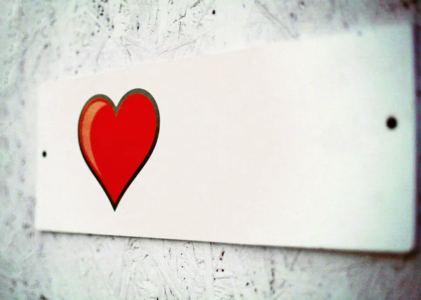 film effect, film grain. a small white plaque on the wall of pressed plywood. beautiful red heart with black edging, Billboard.