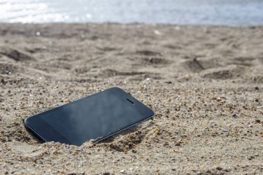 kumda sahilde yatan cep telefonu. hava koşullarına dayanıklı telefonlar, kayıp telefon konsepti, veri kaybı.
