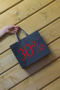 % 30 indirimli siyah hediye alışveriş çantası, ahşap arka planda duruyor..