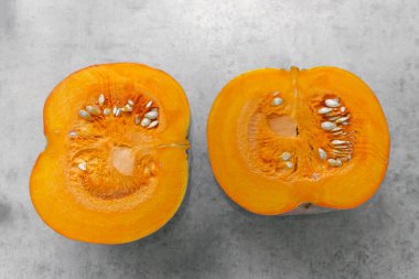 Bir balkabağının iki yarısı gri arka planda ikiye bölünmüş, çekirdek, hamuru ve kabak çekirdeği.