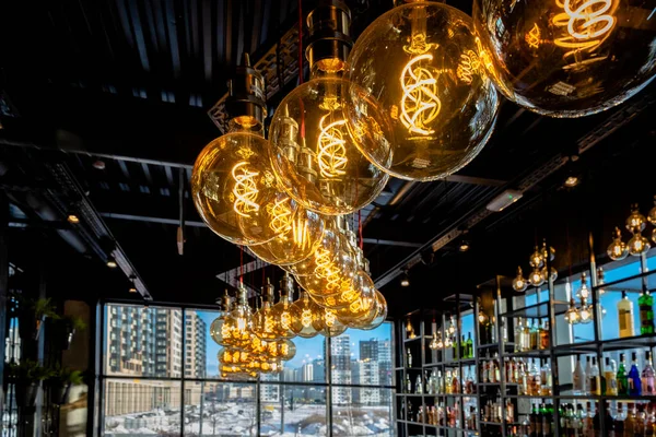 Warm light from beautiful lamps on the ceiling of the bar, against the backdrop of cold lighting from the window on a winter day with a view of the city. drink alcohol and keep warm in the restaurant.