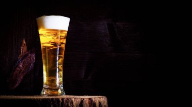 Hafif, köpüklü, siyah ahşap arka planda bir bardakta lezzetli bir bira, tahta testerenin üzerinde duruyor, kenevir..