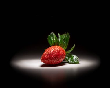 Siyah beyaz arka planda izole edilmiş tek olgun çilek gölgeli beyaz ışık tarafından aydınlatılır..