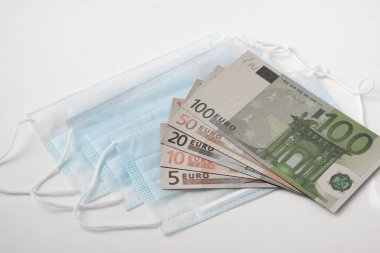 Tıbbi maskeler ve avro banknotları beyaz arka planda izole edilmiş, küresel salgın COVID-19 salgınına karşı ilaç ve ilaç verme kavramı ve Coronavirus ile mücadele.