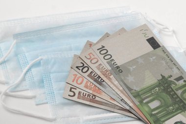 Tıbbi maskeler ve avro banknotları beyaz arka planda izole edilmiş, küresel salgın COVID-19 salgınına karşı ilaç ve ilaç verme kavramı ve Coronavirus ile mücadele.