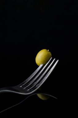 Kemikli yeşil İspanyol zeytini siyah ayna arkaplanındaki izole edilmiş bir çatalla yansıtılıyor..