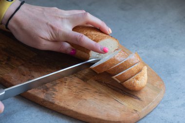 Gri bir tezgahın üzerinde duran uzun ve özel bir tahta üzerinde taze ekmek dilimleme işlemi. Özel ekmek bıçağıyla taze ekmek kes..